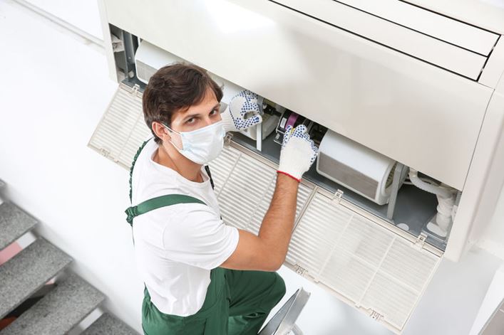 Hombre con mascarilla limpiando un aparato de aire acondicionado
