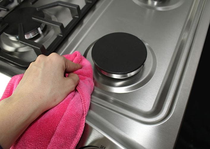 Mano de mujer limpiando una cocina de gas con una bayeta
