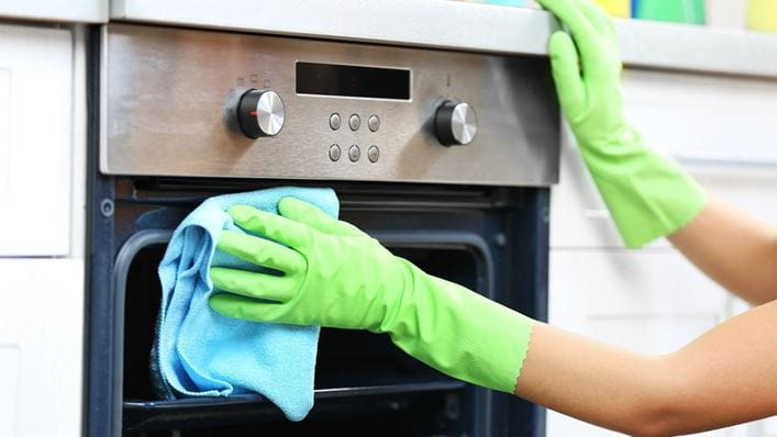 Mujer con guantes limpiando un horno eléctrico