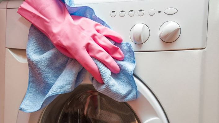 Persona con guantes limpiando una lavadora por fuera